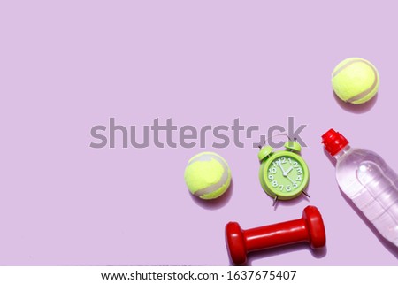 Sports equipment concept. Dumbbells and tennis ball, alarm clock on pastel pink background. Top view copy space.