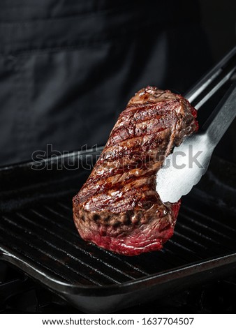 Cooking beef fillet steak on grill pan with salt and pepper on black dark background with copy space text. Food recipe concept.