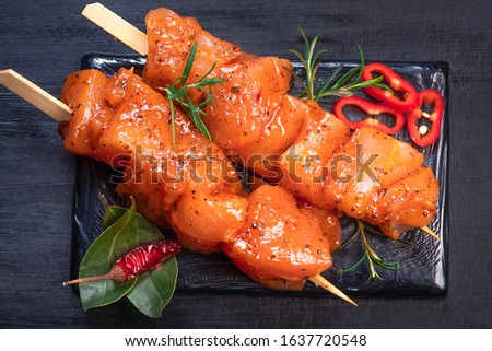Raw chicken skewers in marinade with spices on a black plate and on a wooden table. Raw marinated and spicy chicken skewers.Top view. Chicken meat close up. Raw meat in marinade. Tasting diet meat. Royalty-Free Stock Photo #1637720548