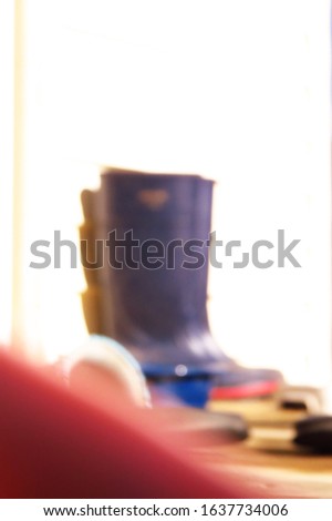 A purposefully blurry, de-focused background of a pair of blue rain boots on a cluttered porch with a red corner at the bottom left of the photo.