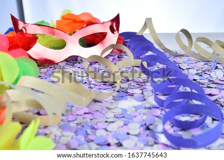 red carnival costume mask on colorful confetti necklace flowers and streamers with space for text