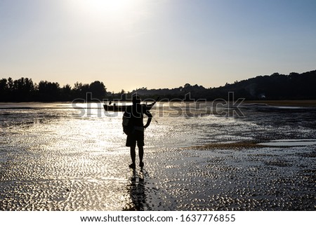 A traveler walking on absandy beach, Heading to a small boat at low tide. In the golden evening sun.