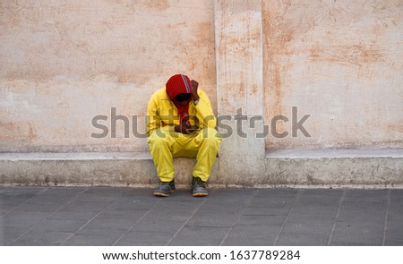 A picture of a wall in Doha Qatar with an unidentified man, a worker, who dressed in a yellow uniform with red headscarf using his phone Royalty-Free Stock Photo #1637789284