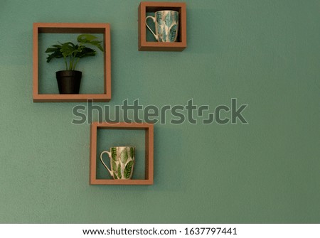 Wooden frame with coffee mugs stuck, tree small on the green wall.