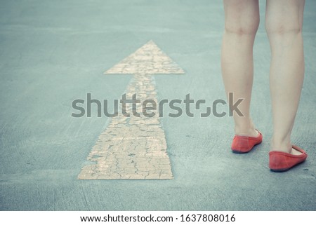 Vintage tone of Girl wear red shoes  walking towards with yellow traffic arrow signage on an asphalt road background