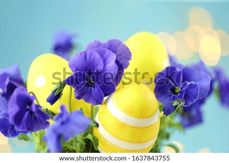 Easter Religious holiday.Yellow decorative easter eggs in blue colors of pansies on a light blue background with yellow bokeh. Spring easter background.