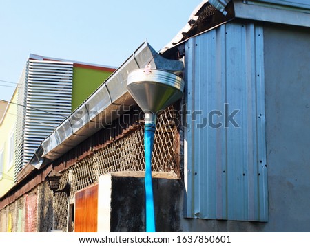 Rainwater pipes and cones connected to the blue rubber pipe on the roof The drainage system is made of zinc for receiving and draining rainwater. On the background of the house wall and blue sky.
