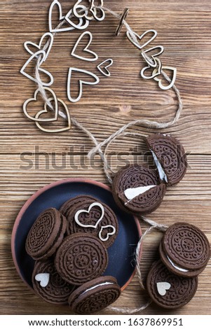 chocolate chip cookie sandwich in a clay plate on a wooden surface. hearts of wood strung on a rope. Happy Valentine's day. Nice picture with a biscuits. wooden background. texture.