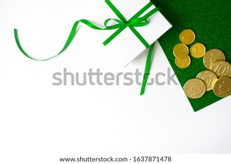 The composition of the St. Patrick's day. White gift box with green bow and gold coins on a green shiny and white background with copy space