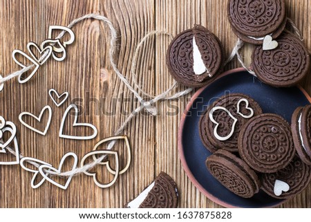 chocolate chip cookie sandwich in a clay plate on a wooden surface. hearts of wood strung on a rope. Happy Valentine's day. Nice picture with biscuits. wooden background. texture.