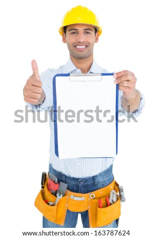 Portrait of a smiling handyman in yellow hard hat with clipboard gesturing thumbs up against white background