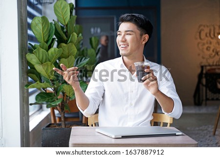 Asian handsome businessman or office worker or young student using laptop computer at office shop with green plant and open space