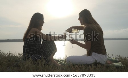 Female couple drinking champagne on a sea shore at sunset