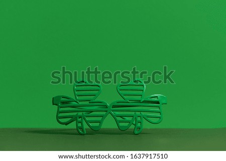 St. Patricks Day in Ireland. Carnival green glasses in the shape of clover on a green background. Empty space for text