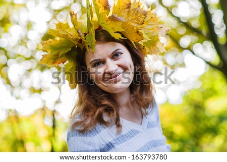 Happy young woman with autumn maple leaves garland in park