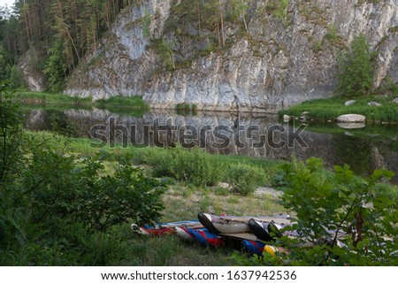 beautiful landscape with catamarans on shore, rock is reflected in mountain river, around forest and green grass