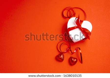 white heart-shaped gift box with red ribbon and candys  for presents or surprises for Valentine's day, international women's day or for celebrating other holidays on red background. Copy space. 