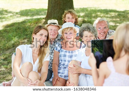 Woman with tablet. Computer takes picture of extended family with child and grandparents in the park