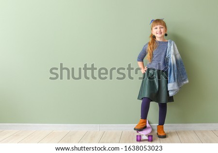 Cute fashionable girl with skateboard on color background
