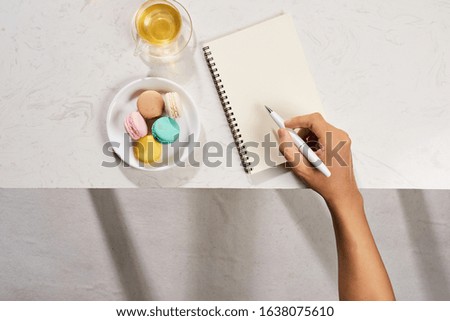 Man writing on notebook with cake macaron and tea mug on white background. Flatlay
