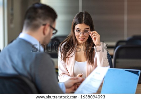 Beautiful female employee in suit is smiling during the job interview. Portrait of young female client or candidate sitting at table, talking to male manager. Job interview or consultancy concept