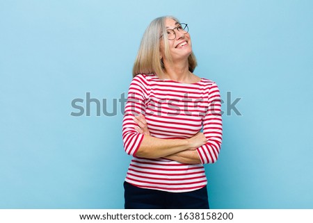 senior or middle age pretty woman feeling happy, proud and hopeful, wondering or thinking, looking up to copy space with crossed arms