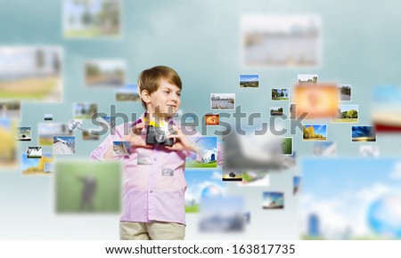 Image of cute boy holding photo camera standing among photos