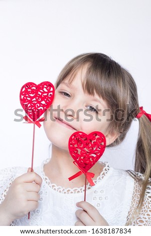Cute girl child holding two decorative red hearts on a stick on white background. Emotion and love concept. Copy space.