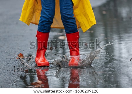 Woman splashing in puddle outdoors on rainy day, closeup