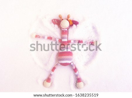 A toy striped pink giraffe lies on the snow, rejoices and wings its paws.
