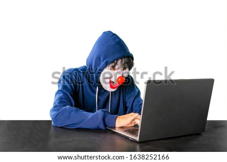 Hacker wearing clown mask using a laptop computer over white background