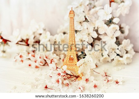 Eiffel tower figurine in flowering branches of cherry and apricot on a light background. Spring in Paris. The atmosphere of romantic travel in the spring.