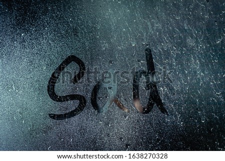 Window with raindrops. Stock photo the inscription "sad" in wet glass.