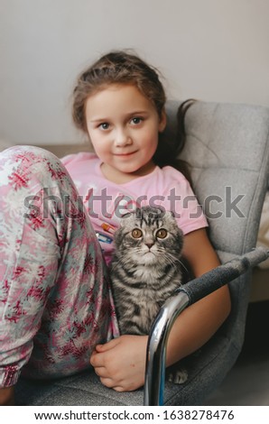 Beautiful scottish fold kitten sits together with little girl and looking to camera. Vertical portrait