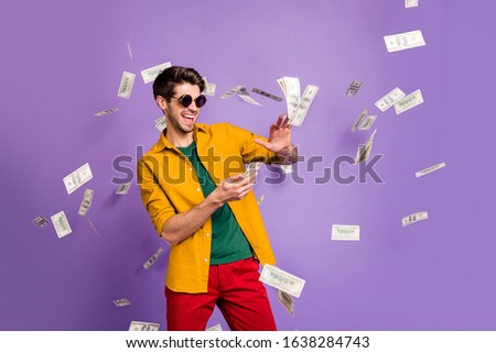 Photo of cheerful excited white trendy man throwing cash away showing his wealthiness smiling toothily in red pants isolated violet color background