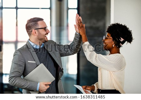 Coworkers celebrating achievement at office. Celebrating success. Happy young man standing in office and giving high five to his colleagues. Two business people high-five. Job well done