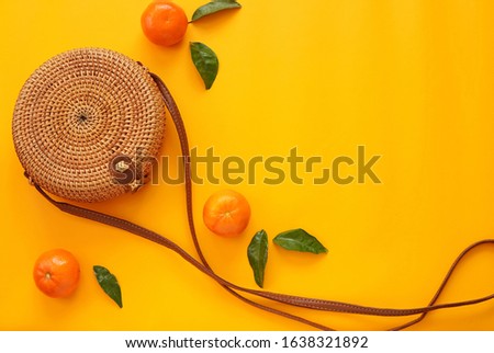 Yellow summertime background, tangerines and round rattan bag, flat lay, vacation, summer fashion concept.