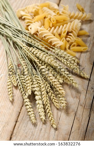 ears of wheat bunch on wooden table with variety of pasta