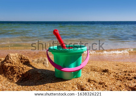 plastic children's toy bucket with a scoop on the sandy shore of the sea beach on a Sunny summer day