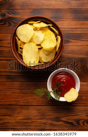 Wavy, potato chips in a plate with ketchup on a wooden table. Top view of snacks. Stock photo potato chips with empty space.
