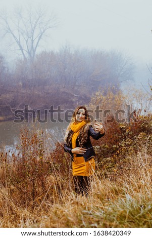 Smiling stylish girl doing selfie in autumn nature near the lake.