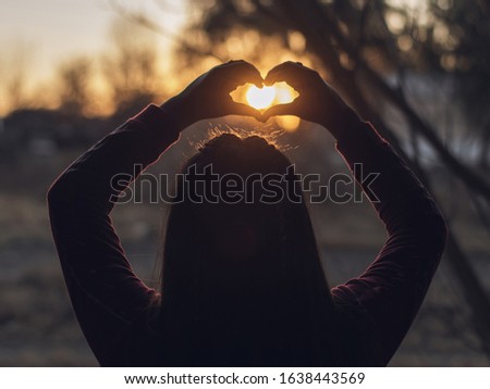 
woman making a heart with her hands in the sunset