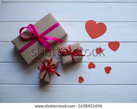 Three present boxes with pink and red ribbons and paper hearts on a white wooden background 