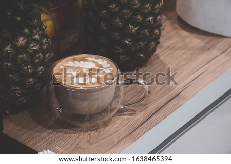 Cappuccino with a picture of a fox in a glass vacuum cup on a wooden table with pineapples on the side.