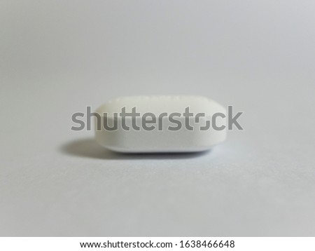 A pill of medicine is placed on white paper. Macro view. Paper texture is seen.