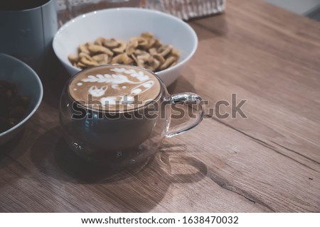 Coffee of cappuccino with FOX picture maked in latte art method in a glass vacuum cup on a wooden table top with bowls with dried fruits next to.