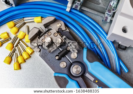 Top view of lying on metal mounting plate wire stripper and blue stranded wire with unused yellow cord end insulated ferrules Royalty-Free Stock Photo #1638488335
