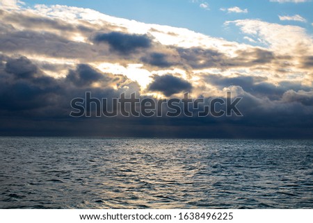 blue dark stormy clouds above the sea, the sun rays breaks through the clouds