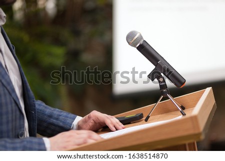 A man stands behind a stand with a microphone and holds a conference Royalty-Free Stock Photo #1638514870