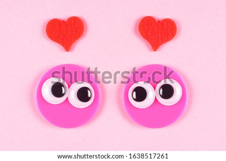 Strange pair of lovers with googly toy eyes on rose background with small hearts. Valentines Day, close up googly eyes.